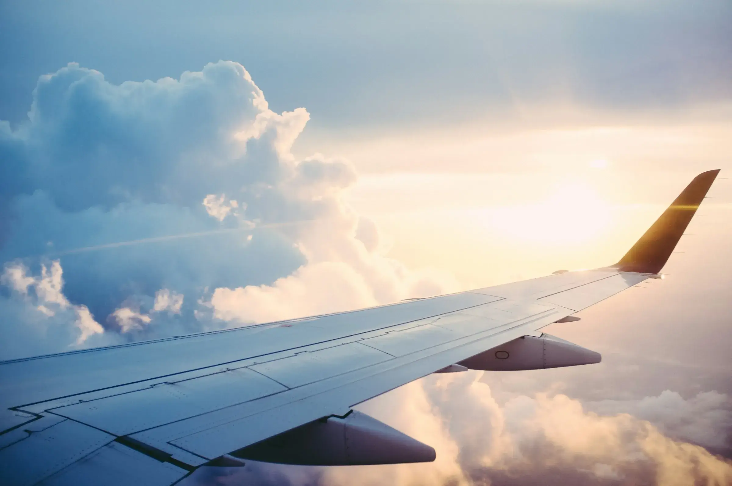 Airplane wing above a sunlit ocean, looking toward distant islands